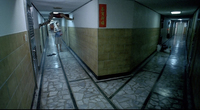 A film still of two hallways diverging from the viewer at the center. To the left, a man braces himself against the walls and ceiling, hanging over another person. To the right, the hallway is empty and poorly lit. A red sign with white calligraphy hangs at the center of the image, at the corner.