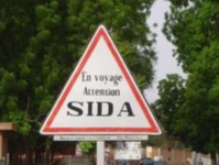 A triangular white road sign with a red outline that reads, on three separate lines, “En voyage / Attention / SIDA.”