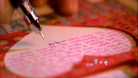 An individual writes pink and blue calligraphy in a heart stencil.