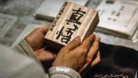 Close up of a character opening a box adorned with calligraphy. The lid is on the table with the character's name, "Shingo," and the character's birthdate.