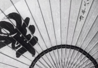 A fan has a large black calligraphy character and smaller black calligraphy written on it, in black and whtie cinematography.
