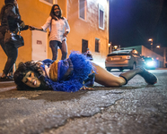 Xandra Ibarra, with a cigarette in her mouth, lies on the street, either getting closer to the pavement or pushing herself up from it.