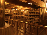 Figure 6 is a photograph of the small-animals exhibit on Deck One of Ark Encounter. Wooden crates of various shapes and sizes line the room, creating a feeling of intimacy within the larger space. Large wooden beams on the ceiling enhance this closed-­in feeling. The room is dimly lit with warm lighting. Some of the light is emitted from simple globes hanging from the ceiling. This lighting further enhances the cozy aesthetic.