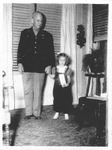 Scan of a black-and-white photograph showing a tall man dressed in uniform and holding the hand of a young girl.