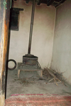 Metal stove with a pipe rising to the ceiling of an adobe house located along Wakhan Valley, Afghanistan. It is dark and gray with little light shining in the space.