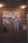 Color photograph of Lewis talking before a podium in a room decorated with baloons and bright colors.