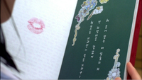 A notebook has lipstick on one side white calligraphy printed inside of a design of flowers.