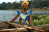 A portrait of a Rwandan woman sitting in a small boat with bananas beside her.