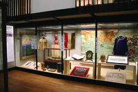Glass-covered cabinet of colonial clothing and objects.