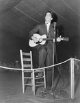 Black-and-white photograph of Alan Lomax singing on a stage with an acoustic guitar