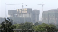 Foggy skyline view featuring trees and an apartment building under construction. Like the factory in the film, the sign atop the building combines calligraphic style on the left with a blocky, font-like "24 City" on the right.