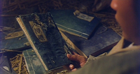 Image of someone holding a blue-covered notebook with black calligraphy on its cover. In the background on the floor, there are several similar notebooks.