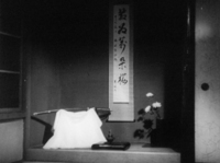 A banner is hanging on the wall with black calligraphy printed on it, in black and white cinematography.