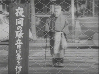 An elderly woman walks behind a fence with a placard with white calligraphy printed on it, in black and white calligraphy.
