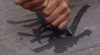 A closeup of a knife carving into calligraphic characters on a wooden surface.