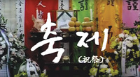 A film still with white calligraphy on a background of a funeral altar and offerings, with multicolored banners behind it.