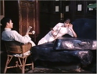 Film still showing a woman in a wheelchair touching a large, smooth stone while a man in a chair watches her.