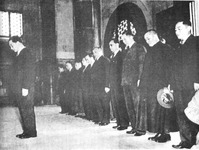 This blurred black-­and-­white photo shows ten men in dark suits or magua jackets standing in one row, with Wang Jingwei alone in front of them, all heads hanging in solemn silence. Zhou Fohai 周佛海, Chu Minyi, Lin Baisheng 林柏生, and Chen Gongbo 陳公博 can be found standing in the middle behind Wang. The hall is otherwise empty and church-­like, with latticed windows and marble half-­columns but no religious symbols.