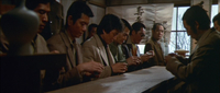 A calligraphic scroll painting and banner are placed over the window, behind a yakuza initiation ceremony—a line of henchmen drinking from sake cups on either side of a long table.