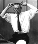 Photograph of Lon Chaney using his hands to lift up pieces of tape attached to the corners of his eyes