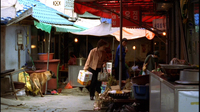 A woman carries a box in an outdoor market, with calligraphy printed o various signs.