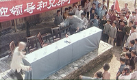 Children gather around a stone dais and draped table, with two adults. A red banner with white calligraphy hangs over it.