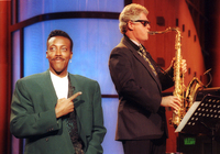 Bill Clinton wearing a suit and sunglasses and playing the saxophone.