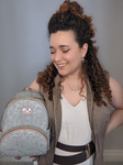 Photo of Samara Trindade wearing a tan vest, beige shirt, brown belt, and Star Wars droid–­inspired gold jewelry. She is smiling and looking down at her mini gray backpack, which has a droid-­inspired allover silver and bronze print.