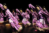 Eleven women dancers in lavender Han dynasty-style Chinese robes poise mid-step, their bodies and arms forming diagonal lines, about to step on round floor drums.