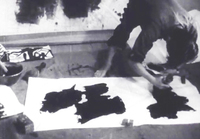 A woman bows painting large black calligraphy on paper, in black and white cinematography.