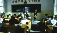 A man stands in front of a classroom with a slogan written on the wall above the chalkboard.