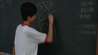 A student draws yellow calligraphy on a chalkboard.