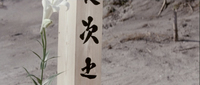Black calligraphy on a wooden post, alongside a white flower.