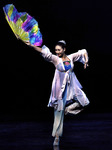 Figure 12.1. A woman dancer in flowing pants and jacket poises on the ball of her right foot, lifting into the air as she reaches up to the right with an open rainbow-colored silk fan.