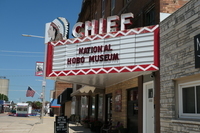 Fig. 20. An old red-and-white movie marquee with the word “Chief” on top features the sign, “National Hobo Museum.” A sidewalk sign advertises the gift shop, and an American flag can be seen down the street.