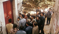 People gather in front of a red door, with yellow calligraphy.