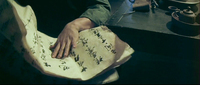 Close-up image of a hand folding large pieces of paper that have black handwritten calligraphy on them.