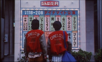 Two young men look at a glass display with red, white and black calligraphy printed on it.