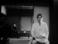 Front-view black and white image of a man kneeling near a doorway and holding a large piece of paper that has calligraphy on it.