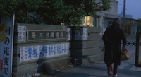 A character walks past a wall with the metal, calligraphic signage, and several protest signs. One says, "Stop wasting electricity."