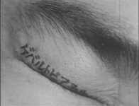 A film still of calligraphic text painted along the edge of a closed eyelid.