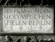 German text and numerals are carved in stone, in black and white cinematography.