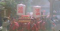 Hazy image of a group of people in red uniforms parading toward the viewer. Some are holding large lanterns with red calligraphy printed on them.