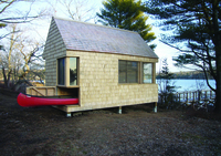A photograph of a small wooden studio on the water. A shelf in the bottom corner holds a canoe.