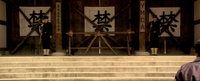 Two soldiers stand at the top of stone stairs, guarding a barricaded doorway. Calligraphy is visible on signs and banners.