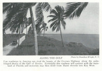 The image depicts a car making its way along the new Oversea Highway. Palm trees appear on the right between the road and the ocean.