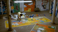 Basquiat paints and writes on a canvas spread on the floor.