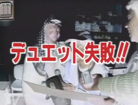 Color still. Image shows man and women in negative (colors reversed). In foreground, Japanese text reads: “Duet fail!!”