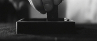 A hand puts a brush in ink in close-up, in black and white cinematography.
