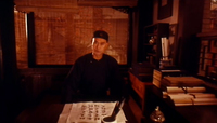 A man sits in front of a desk with black calliraphy written on paper.